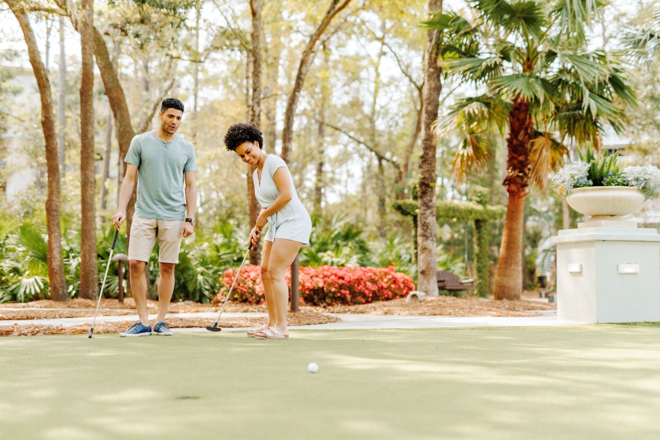 5.	A couple play mini golf surrounded by palm trees and flowers.