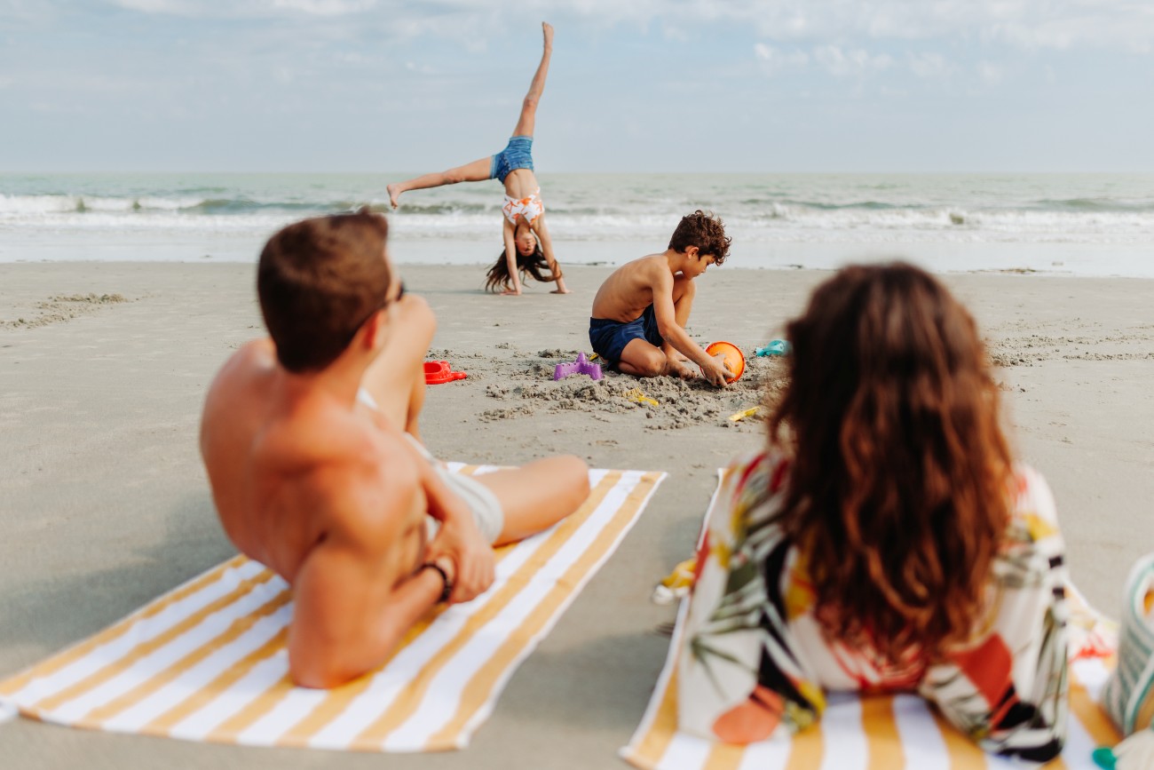 6.	A young girl does a cartwheel on the beach as a boy plays in the sand and a couple sit on towels overlooking the ocean. 