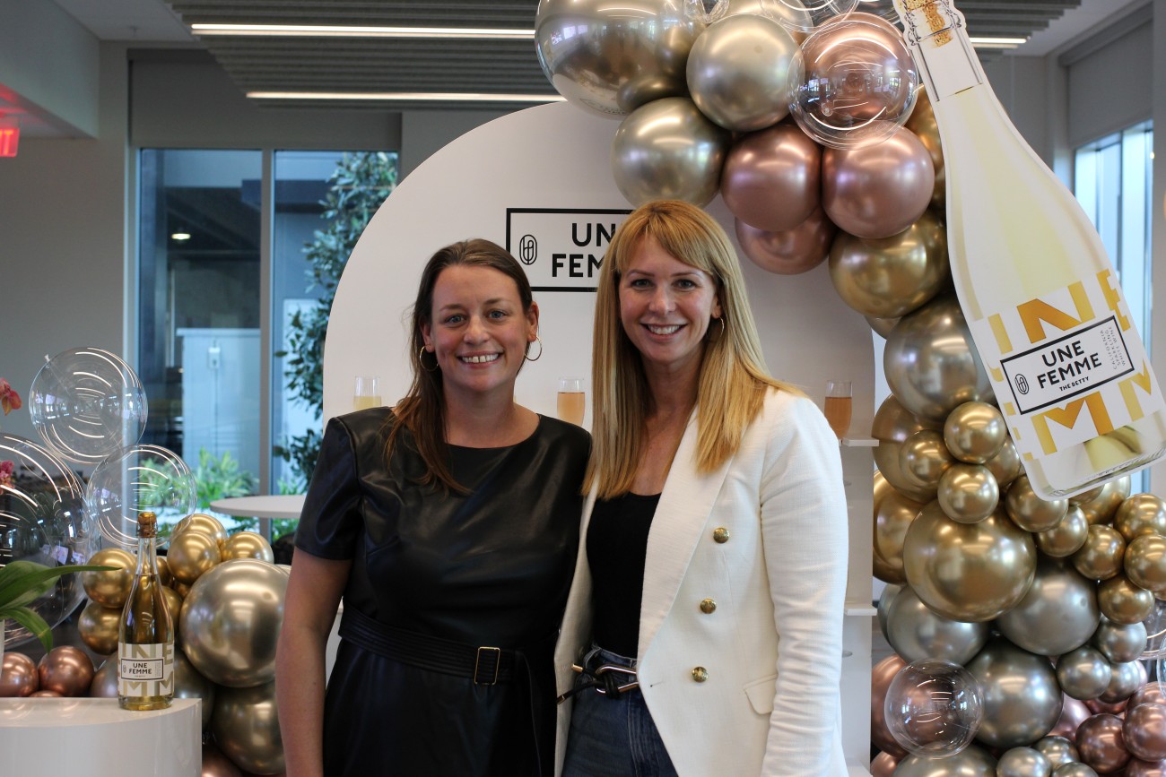 1)	Jen Pelka and Lori Gustafson stand in front of a floral backdrop for Une Femme.