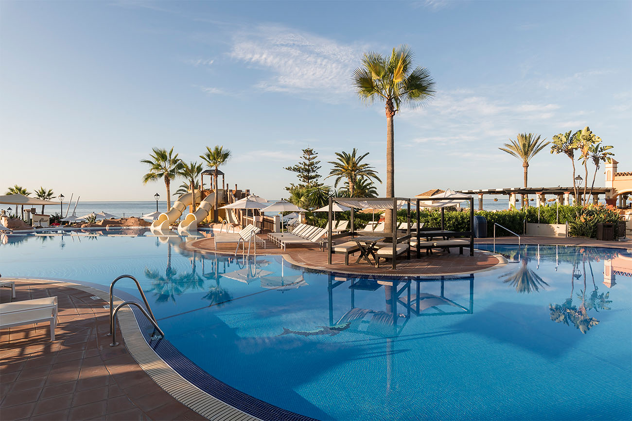 A calm pool reflects the blue Spanish sky and friendly palm trees.