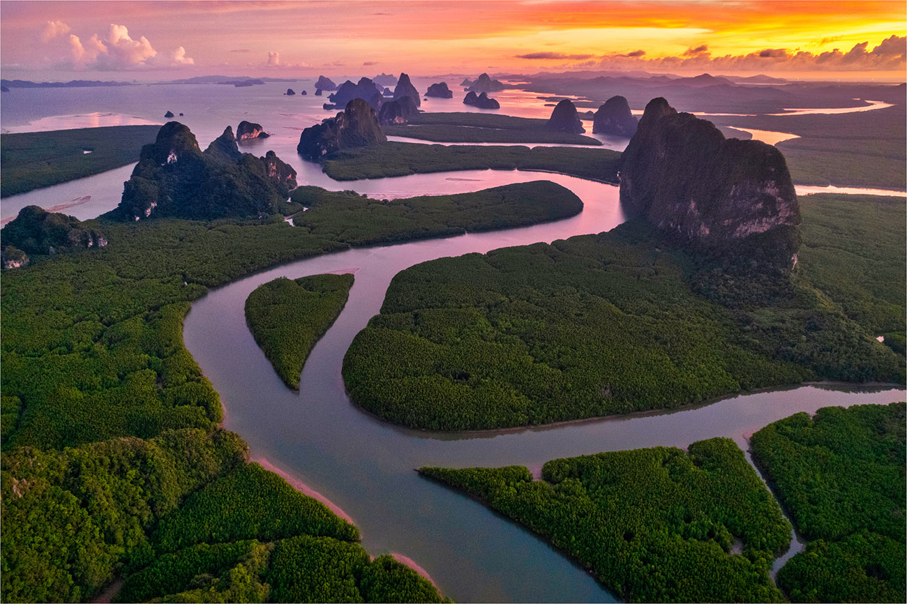 An aerial shot shows winding waterways lined with vegetation during sunset.