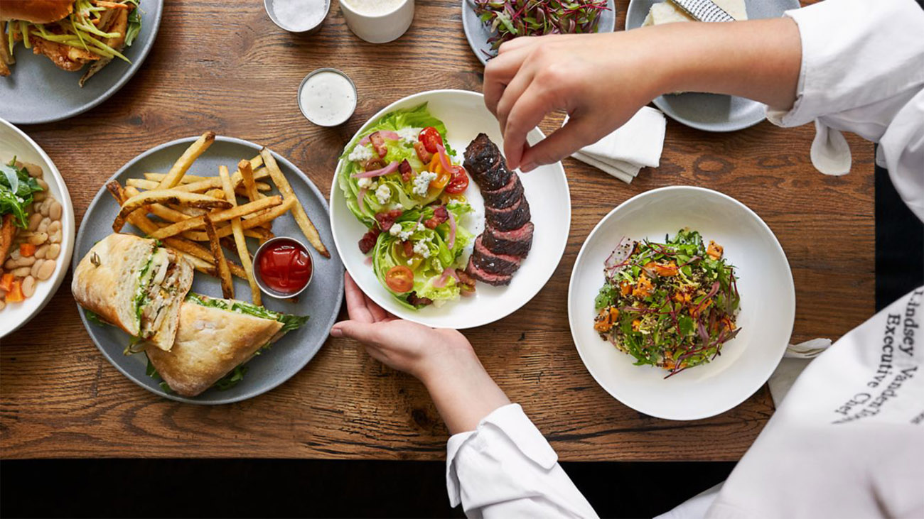 Two plates of salad are being placed on a table filled with food.