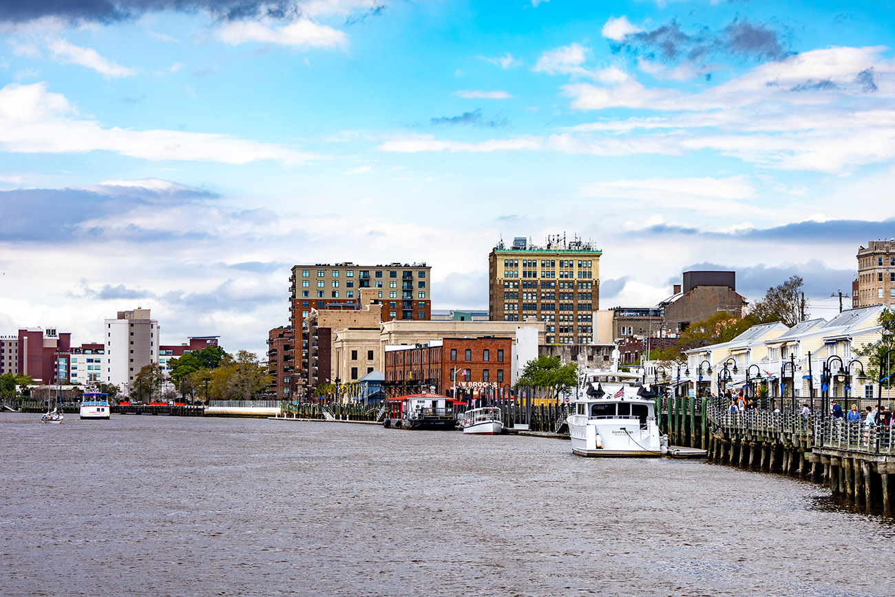 Waterfront scene in Wilmington with boats docked at a marina and historic buildings along the shoreline.