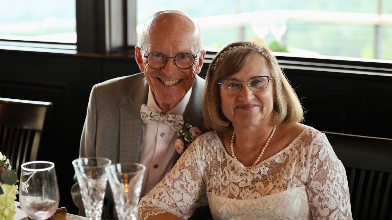 Newlyweds Andy Boye and Lori Kruczek pose smiling in front of historic stone buildings.