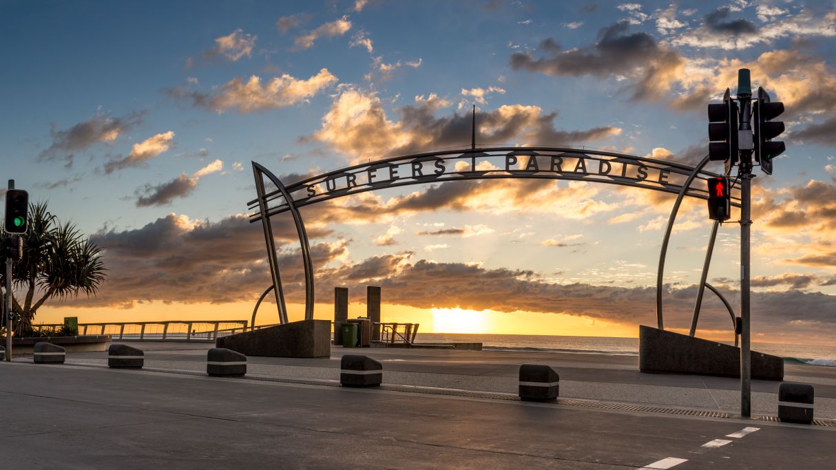 The sun begins to set behind the archway sign at the entrance to Surfers Paradise Beach.