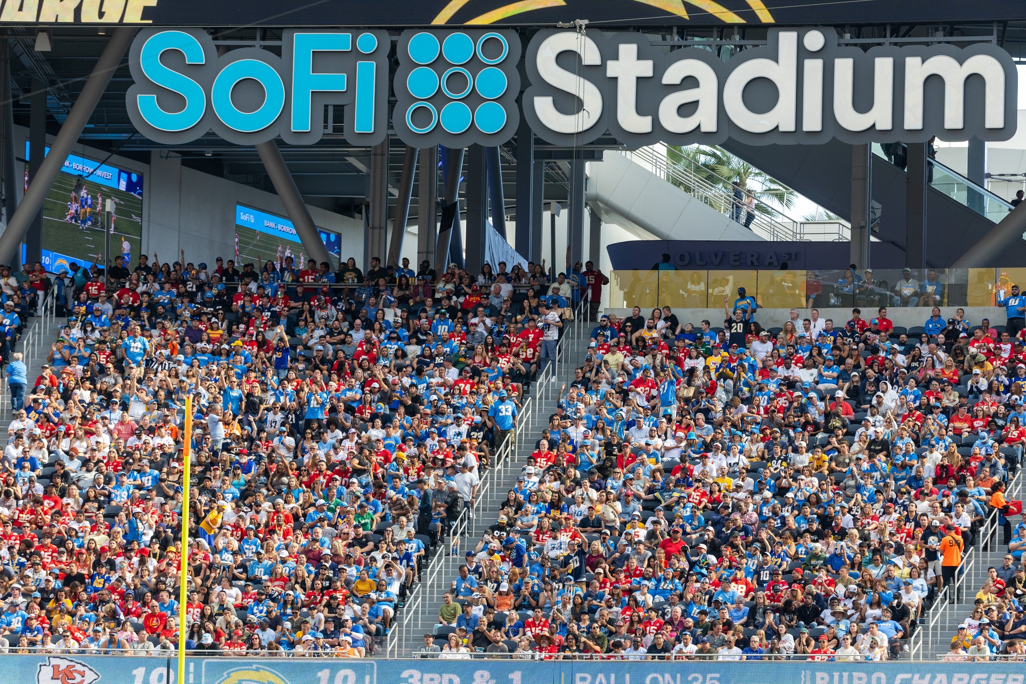 A group of fans loudly cheer with their hands in the air at a soccer game.