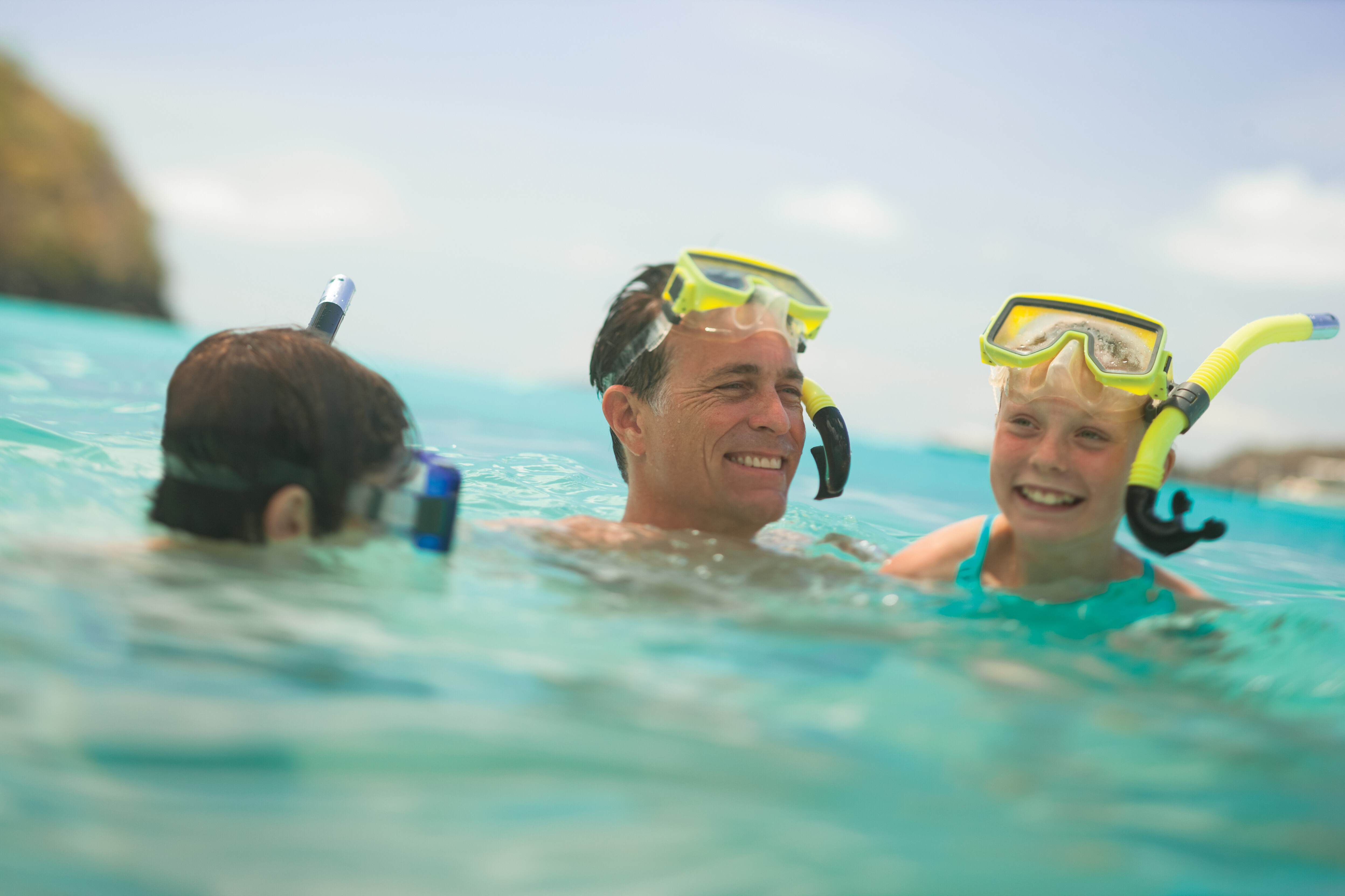 A father snorkeling in the ocean with his children. 