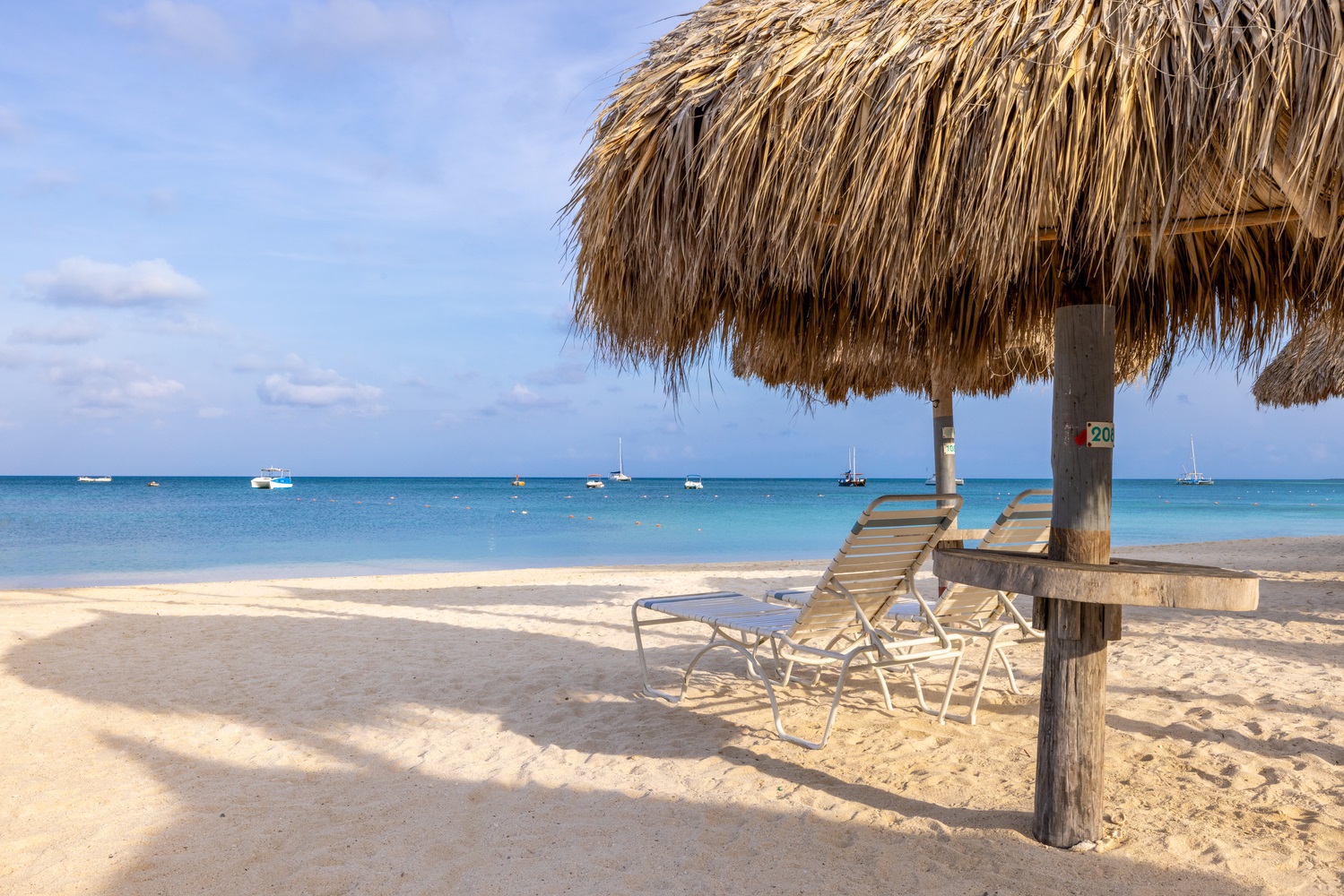 Sandy beach with two empty lounge chairs under a thatched palapa. 