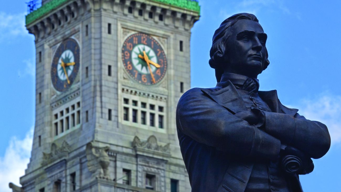 The historic clock tower in Boston stands beside a commemorative statue. 