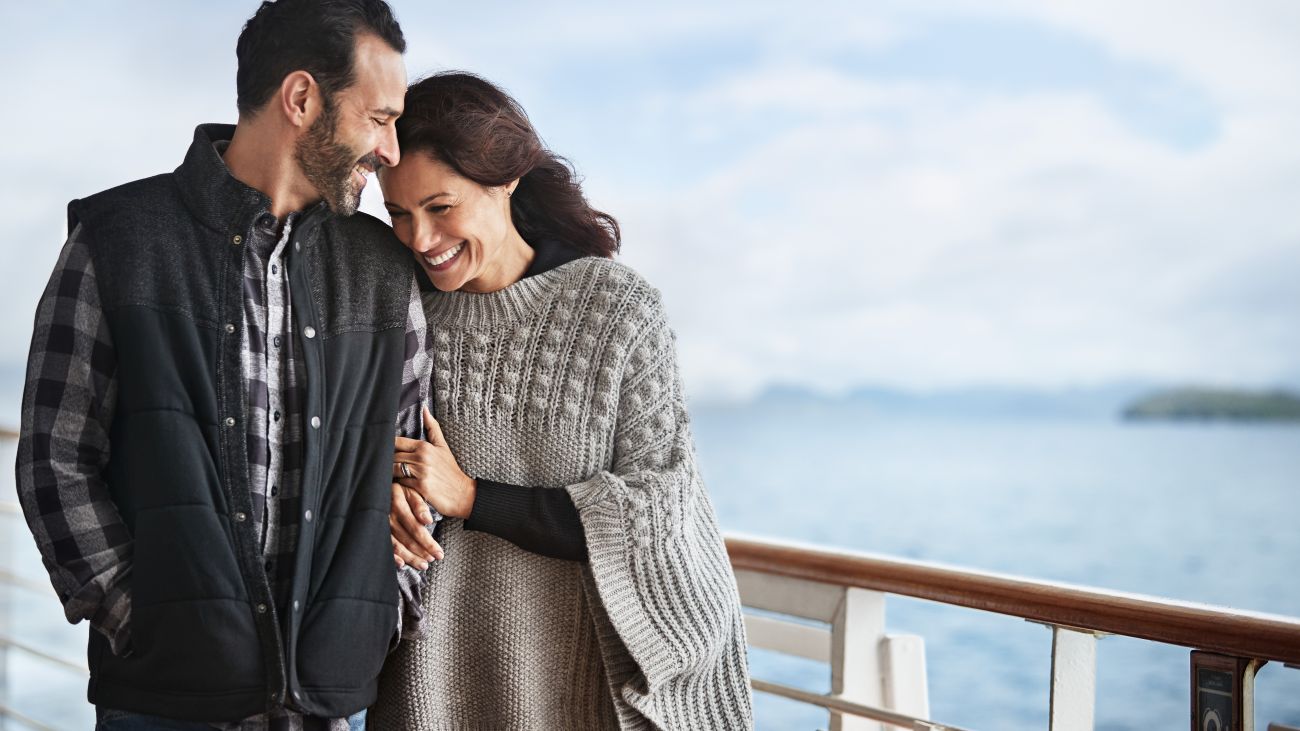 Two people stand on a cruise ship deck looking out over the ocean. 