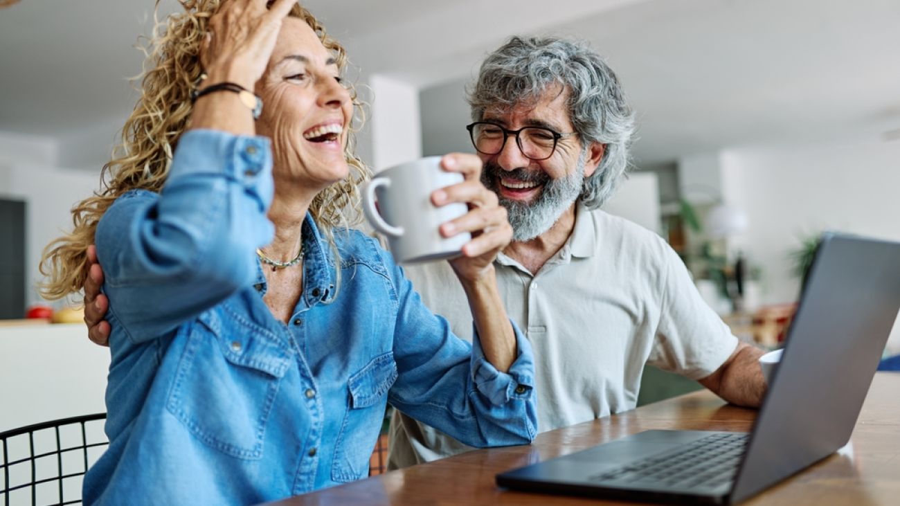 A couple sits at a home computer desk with an open laptop.