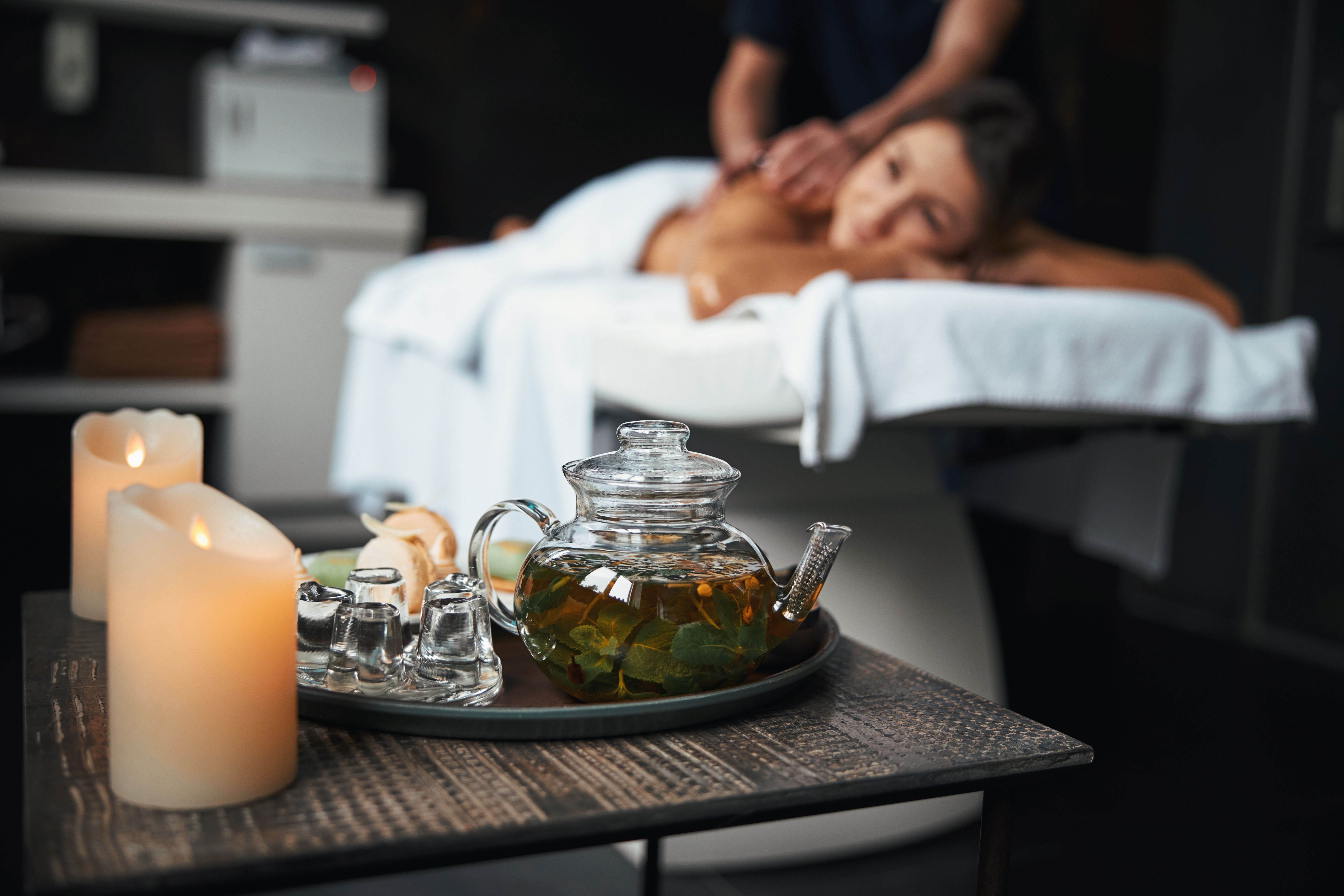 A person lies on a spa treatment table with lit candles and massage oils. 