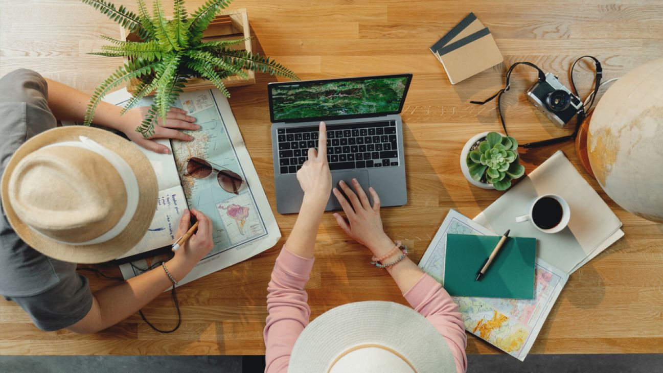 A person works on a laptop with a notebook, camera, and coffee nearby.